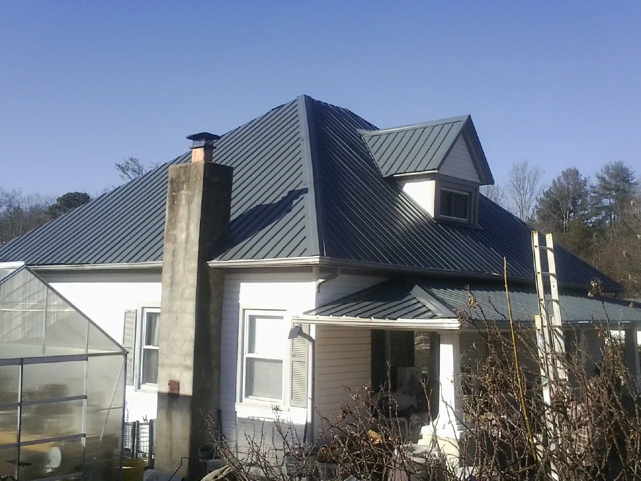 Dark blue standing seam metal roof on a white farmhouse with dormer — Slate & Tile Roof Repair by Roofing Brothers in East Greenville
