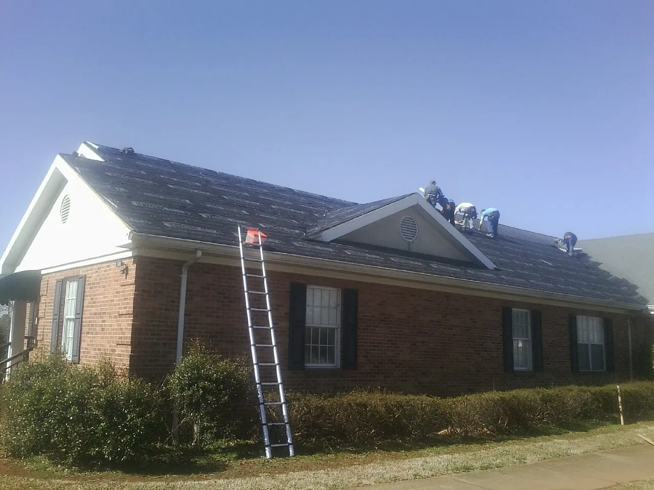Crew tearing shingles off a brick ranch roof with a ladder set — Metal Roof Repair work by our crew in East Greenville