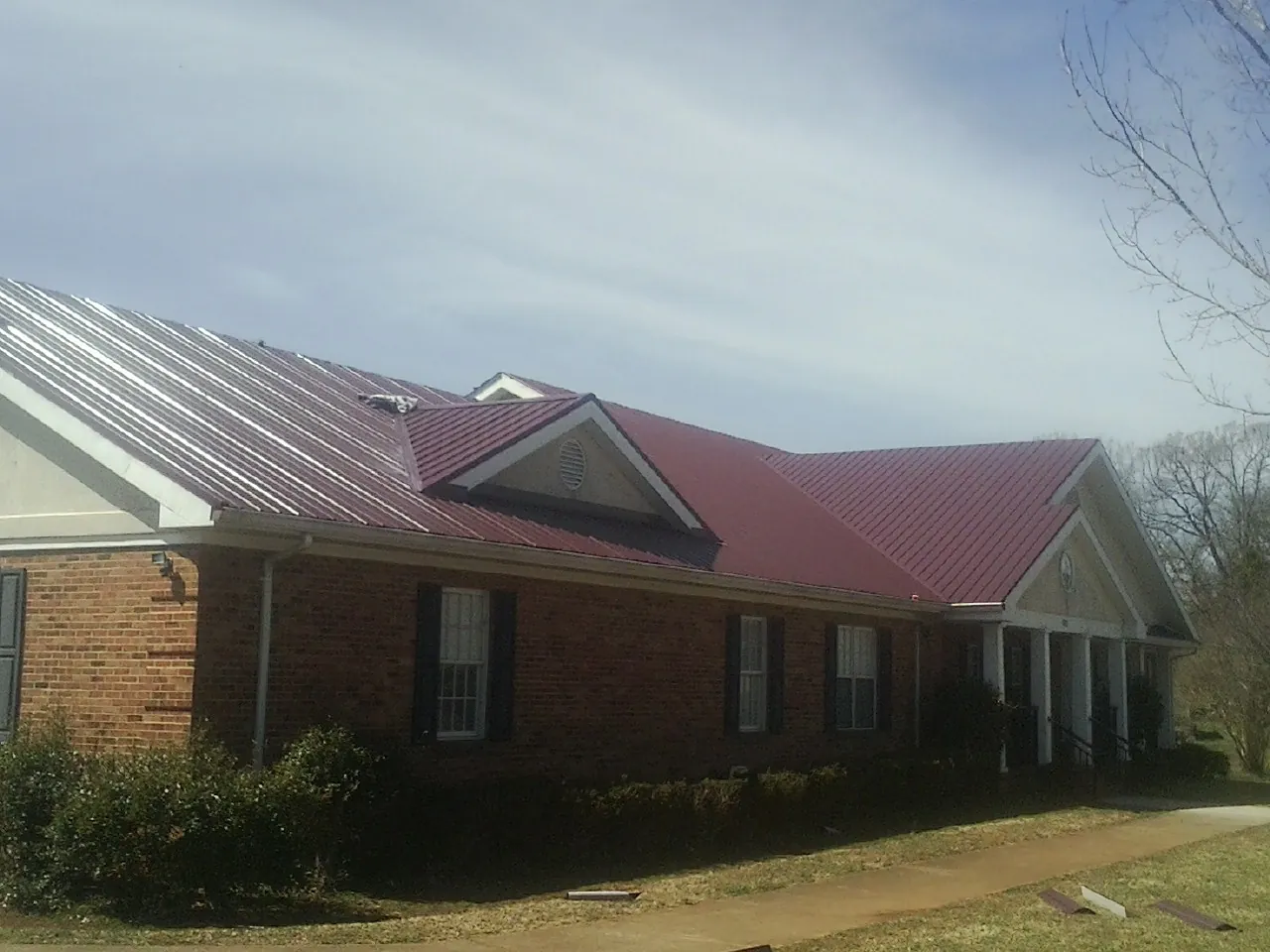 Red metal roof with gabled entries on a long brick building, from a Hail Damage Roof Repair job in East Greenville