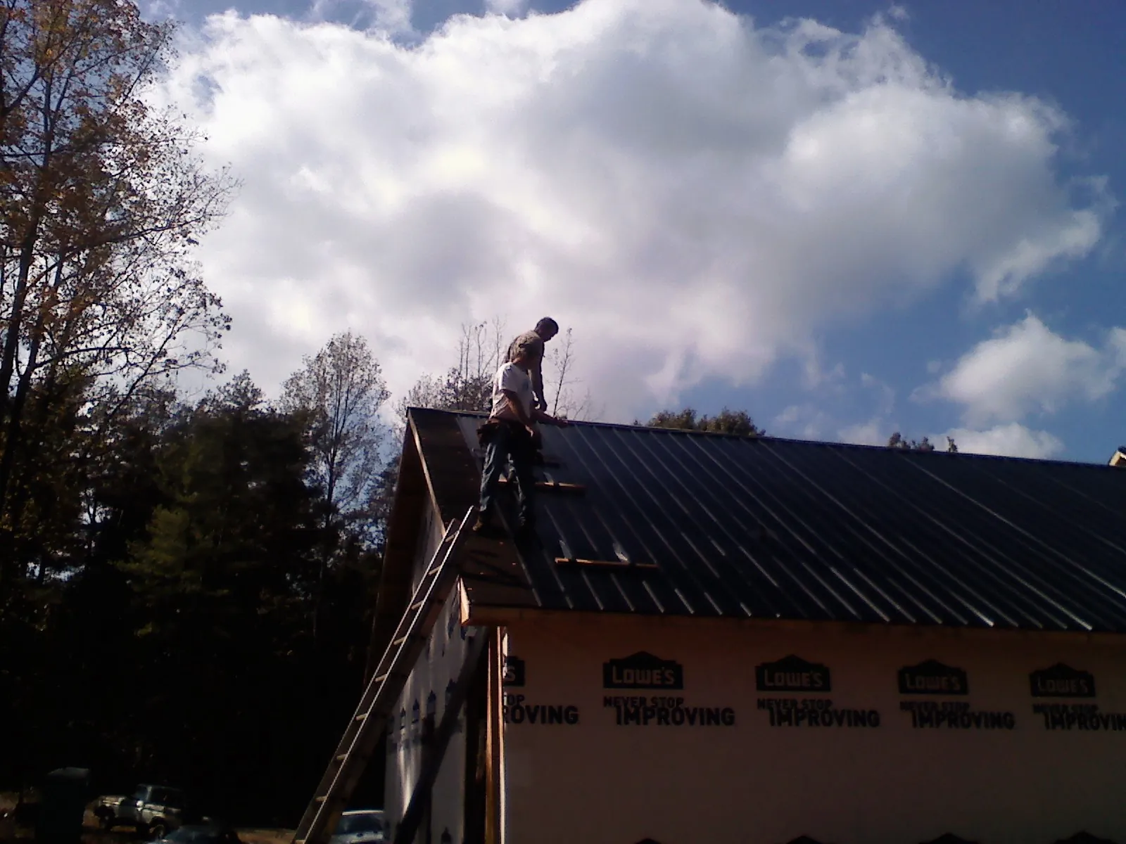 Roofer fastening dark metal panels high against a cloudy sky, from a Roof Inspection job in East Greenville
