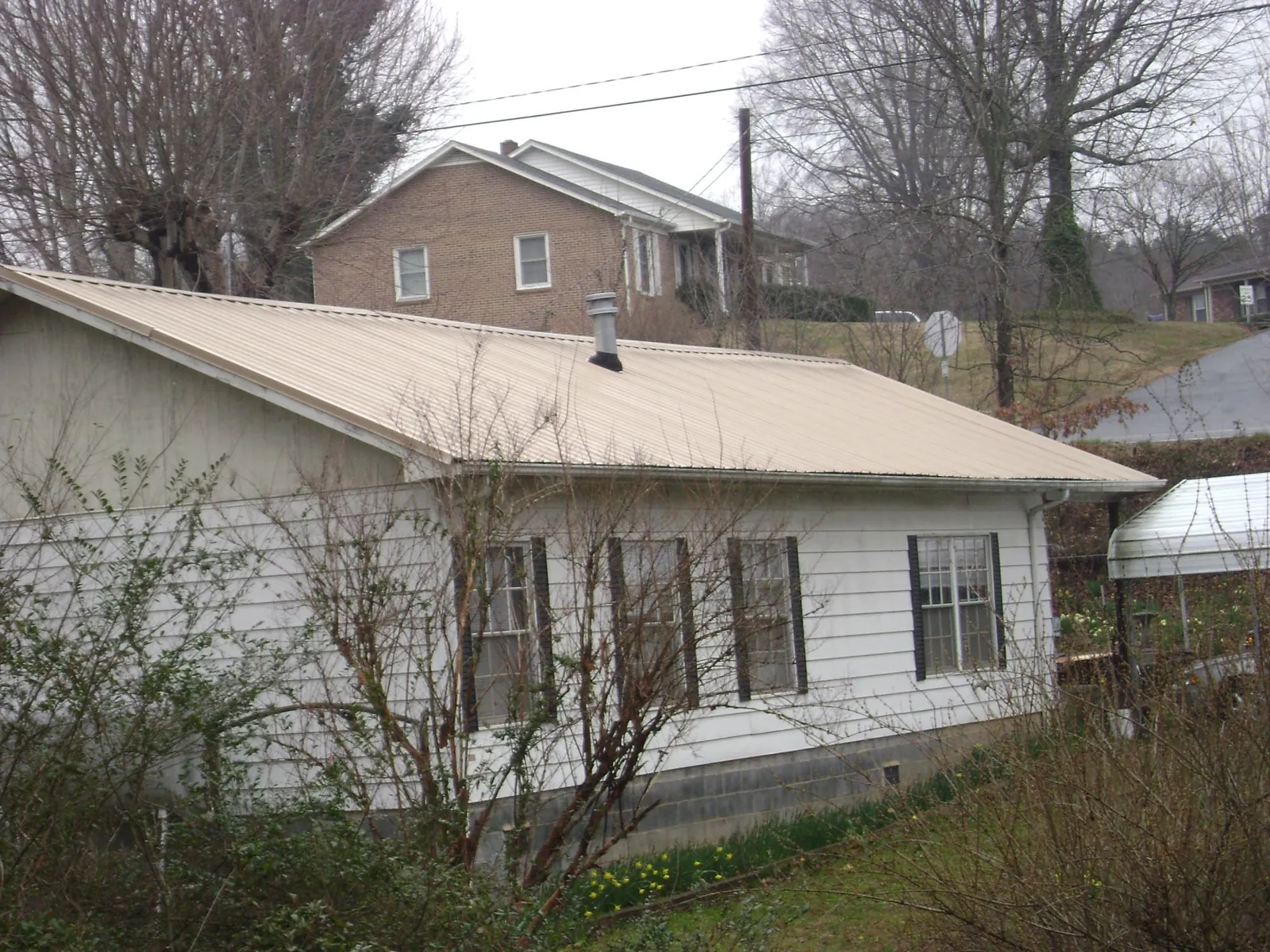 Tan metal roof on a white sided house set into a hillside — Commercial Roofing by Roofing Brothers in East Greenville