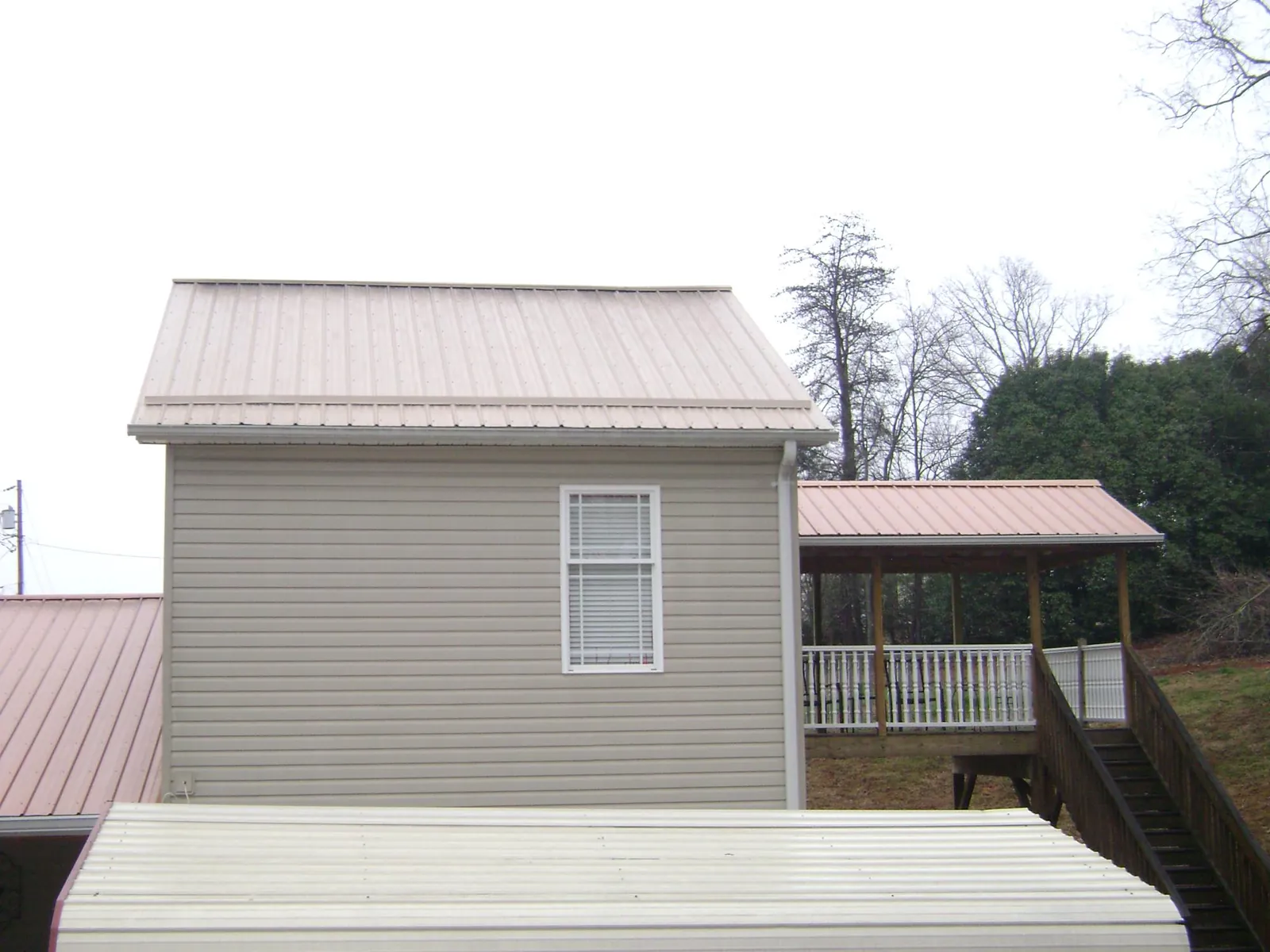 Tan metal roofs on a two story addition and attached porch, from a Roof Replacement job in East Greenville